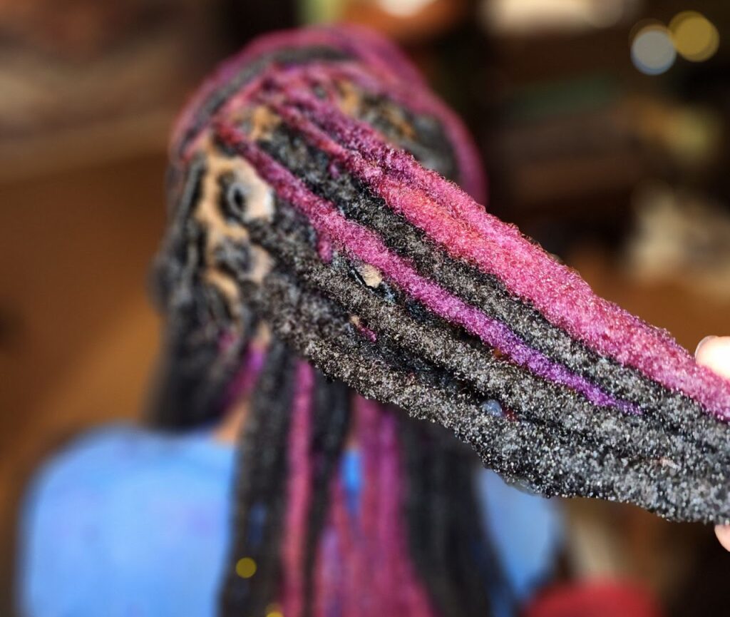 A photo of a hairstylist showing their work done on a client. Loc hair coloring.